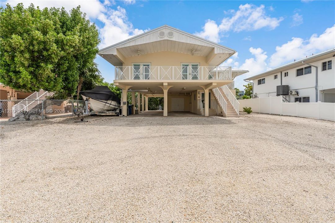 Stilt-construction home featuring a gravel driveway, an elevated deck with metal railing, and exterior stairs