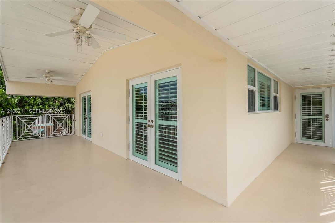Covered porch featuring painted beadboard ceilings, ceiling fans, multiple sets of glass-paneled double doors, interior shutters, and a decorative metal railing