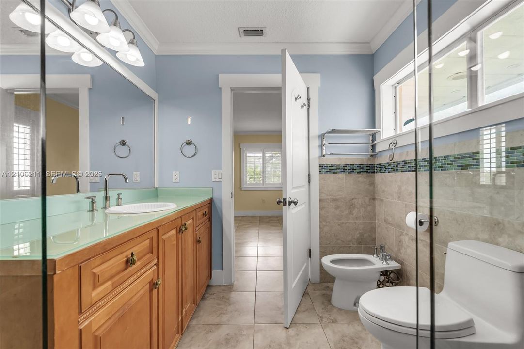 Bathroom featuring a wood vanity with a glass countertop, integrated sink, stone tile flooring, wall-mounted bidet, and mosaic tile accent border