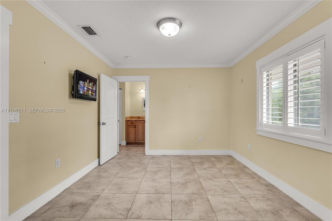 Room featuring large-format ceramic tile flooring, crown molding, plantation shutters, and a classic arched-panel interior door