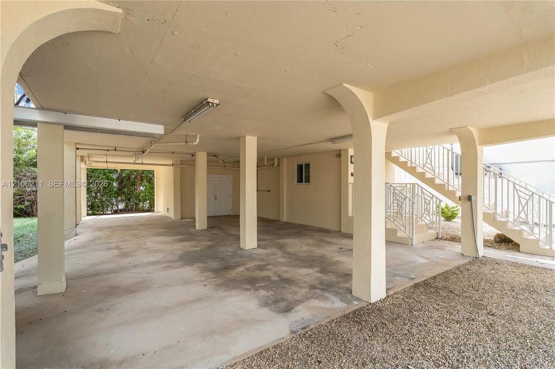 Covered parking area featuring structural pillars, concrete flooring, and metal railings on the external staircase