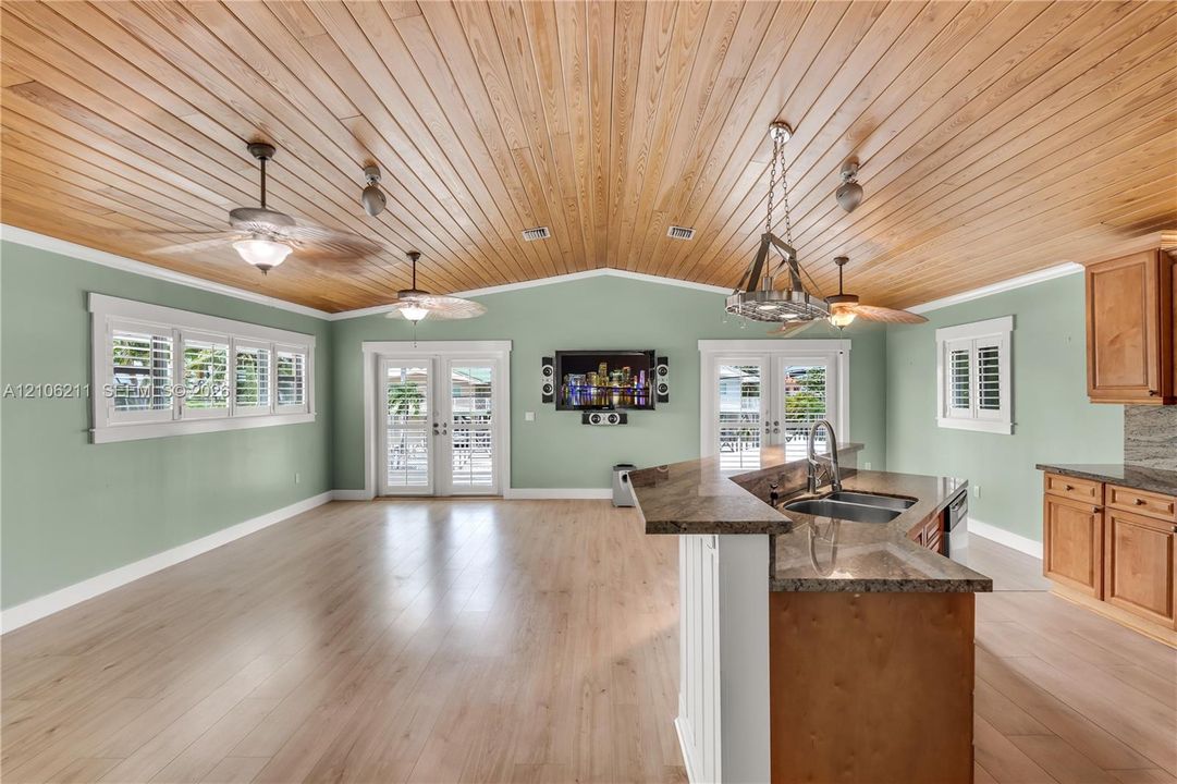 Vaulted wood-plank ceiling, wood-finish flooring, kitchen island with stone countertop, stainless steel dual-basin undermount sink, and multi-pane French doors