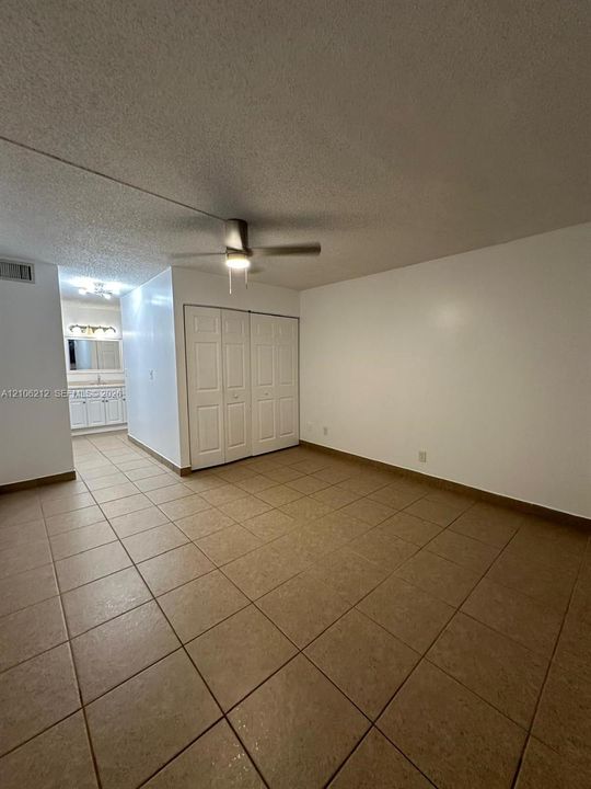Neutral-toned ceramic tile flooring, ceiling fan with integrated lighting, dual-panel closet doors, and multi-light vanity fixture