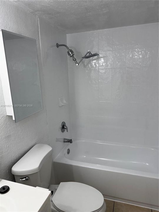 Full bathroom featuring a white porcelain tub with integrated tile surround, wall-mounted shower head, recessed soap dish, and mirrored medicine cabinet