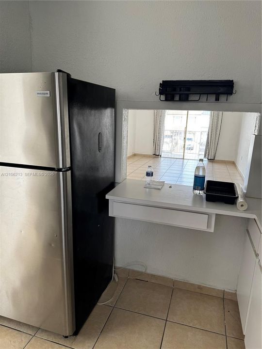 Stainless steel refrigerator with a black finish, ceramic tile flooring, and a built-in pass-through service counter featuring a storage drawer