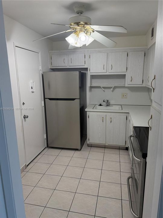 Kitchen featuring light-finish cabinetry, stainless steel refrigerator, integrated range, ceramic tile flooring, and a ceiling fan with integrated lighting