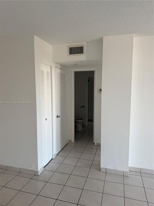 Interior space featuring neutral tile flooring and two sets of louvered-style closet doors
