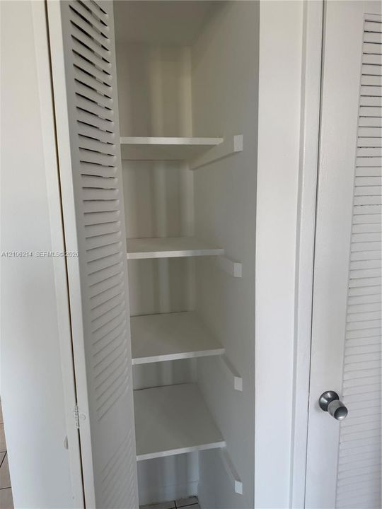 Storage closet featuring white louvered doors and four fixed interior shelves