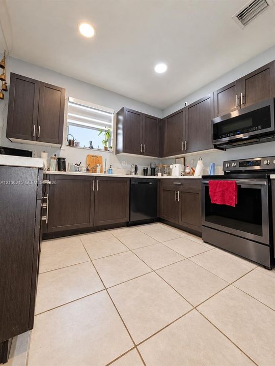 Kitchen featuring dark-finish cabinetry, solid-surface countertops, large-format tile flooring, and stainless steel appliances including a built-in microwave and range