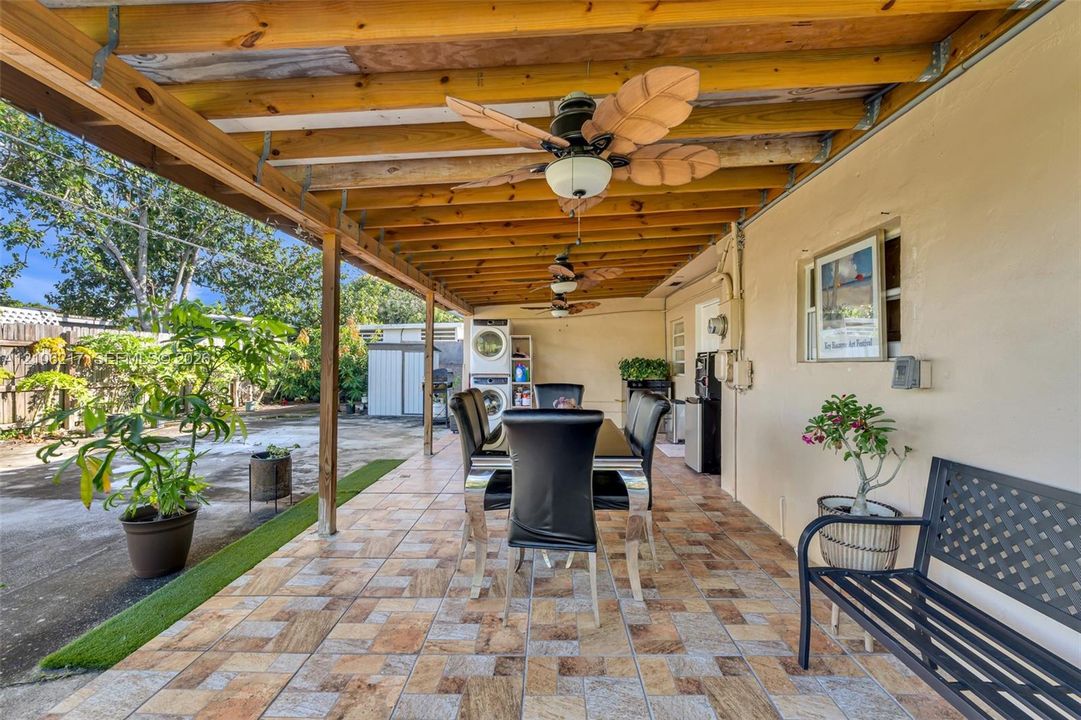 Covered patio featuring patterned tile flooring, exposed wood-beam ceiling, and multiple ceiling fans