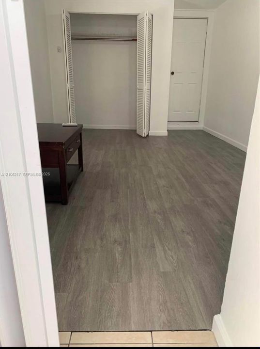 Neutral-toned wood-finish flooring, white walls, and a closet with bifold doors
