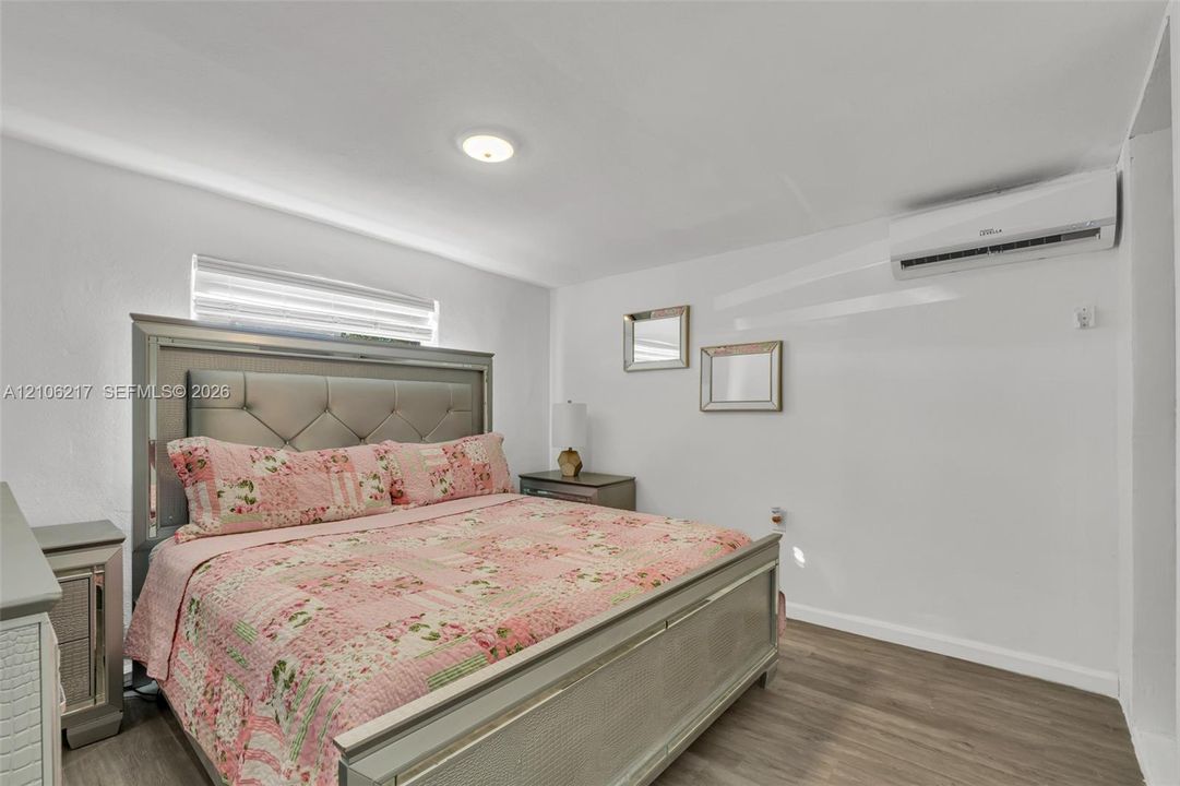 Neutral-toned room featuring wood-finish flooring, a wall-mounted ductless air conditioning unit, and a window with horizontal blinds