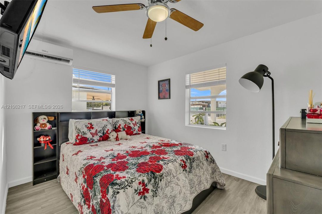 Room featuring wood-finish flooring, a wall-mounted ductless air conditioning unit, and a ceiling fan with integrated lighting