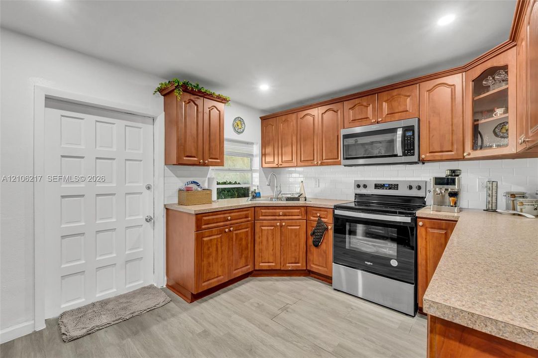 Kitchen featuring wood cabinetry, stainless steel appliances, white subway tile backsplash, solid surface countertops, and wood-finish flooring
