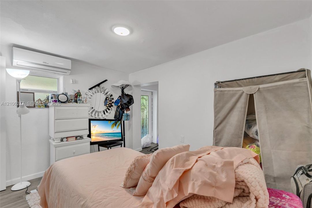 Wall-mounted ductless air conditioning unit, ceiling-mounted flush light fixture, and glass-paneled exterior entry door with decorative metal grill