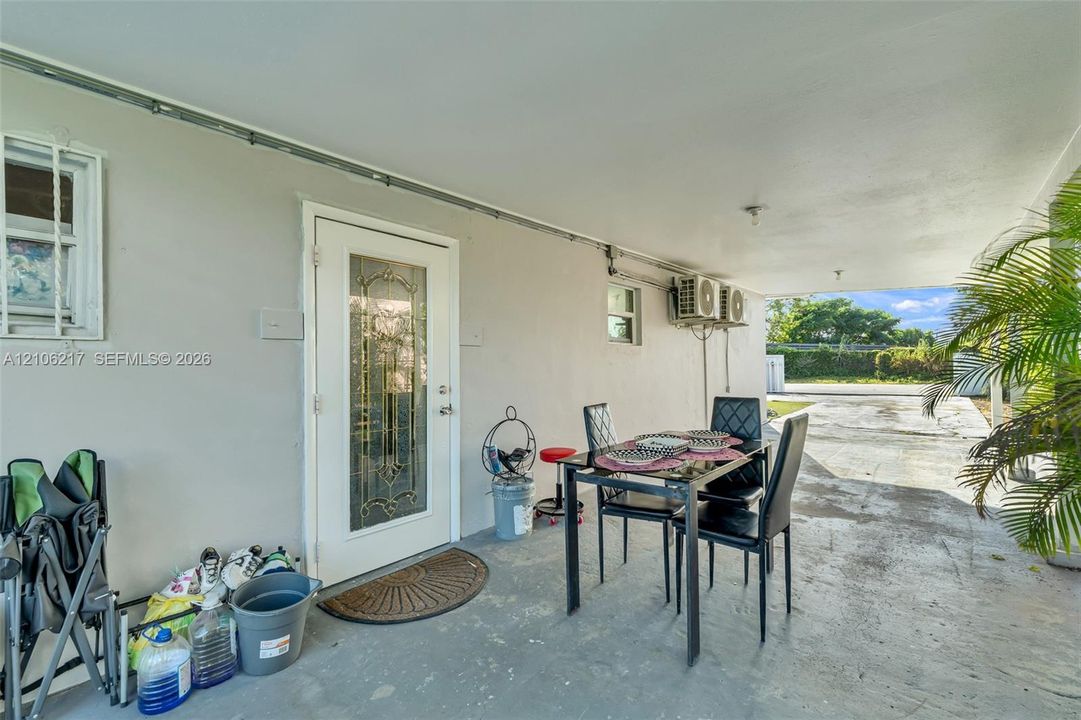 Covered concrete patio featuring a glass-panel entry door and exterior wall-mounted cooling units