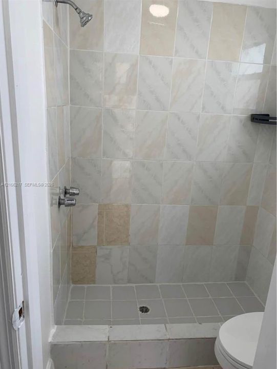 Walk-in shower enclosure featuring light-toned decorative wall tile, a square-tiled basin, and a metal shower head and handle set