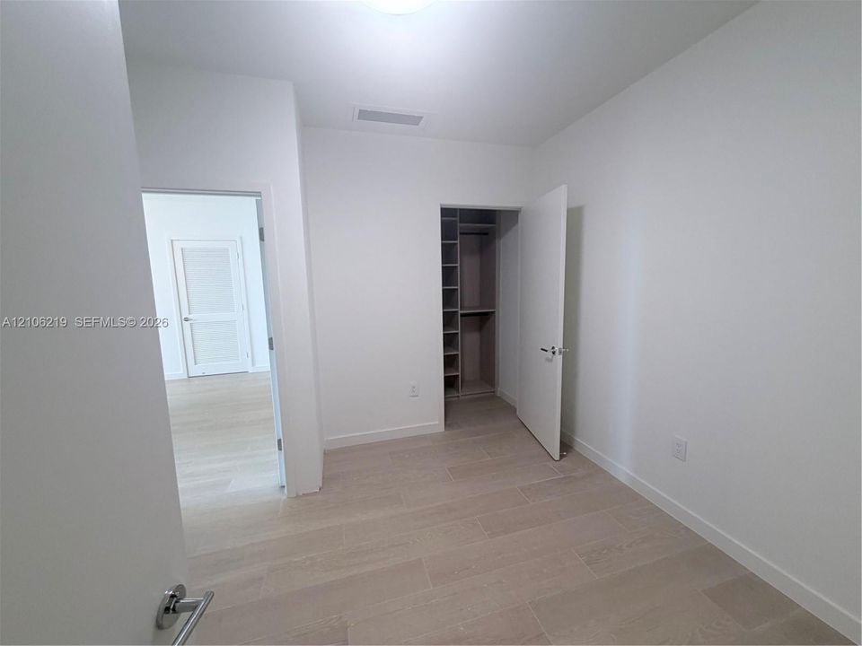 Neutral interior featuring large-format tile flooring and a walk-in closet with custom built-in shelving