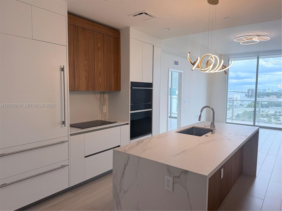 Modern kitchen featuring floor-to-ceiling cabinetry, integrated appliances, a central island with a stone-finish countertop, and floor-to-ceiling windows