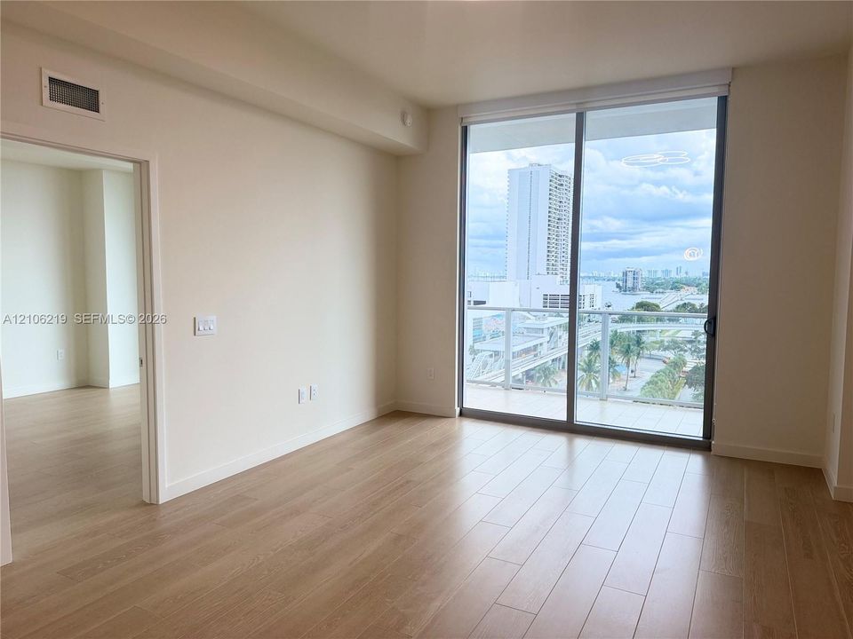Floor-to-ceiling glass sliding door, light-toned wood-finish flooring, and private balcony with glass railing