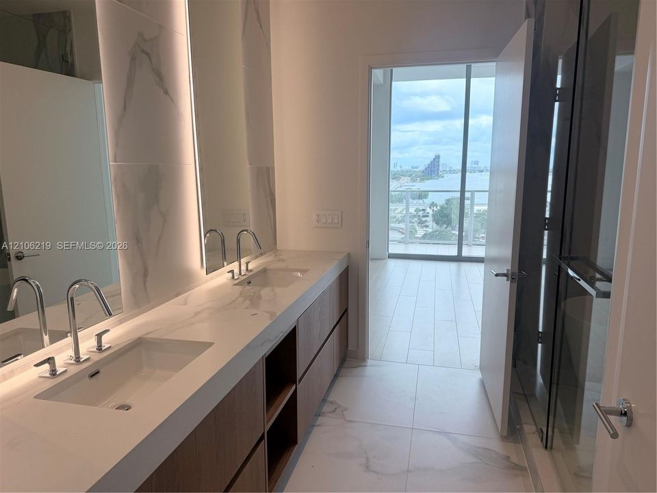 Double vanity with integrated sinks, stone-finish countertops, wood-finish cabinetry, floor-to-ceiling tiled backsplash, and glass-enclosed shower