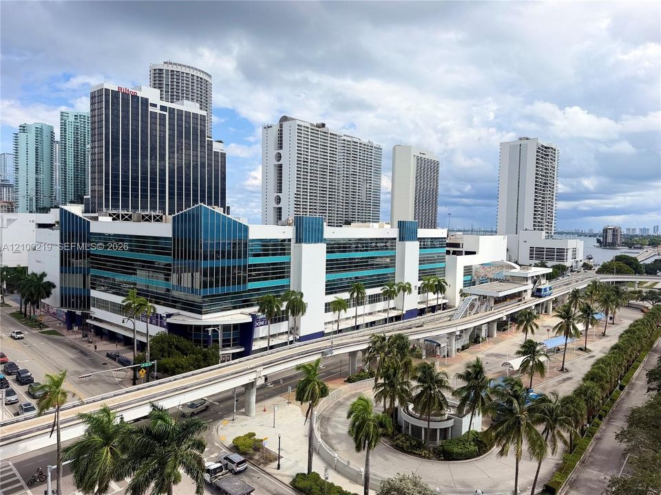 Urban aerial perspective featuring multi-story commercial architecture, integrated rail infrastructure, and palm-lined hardscaping