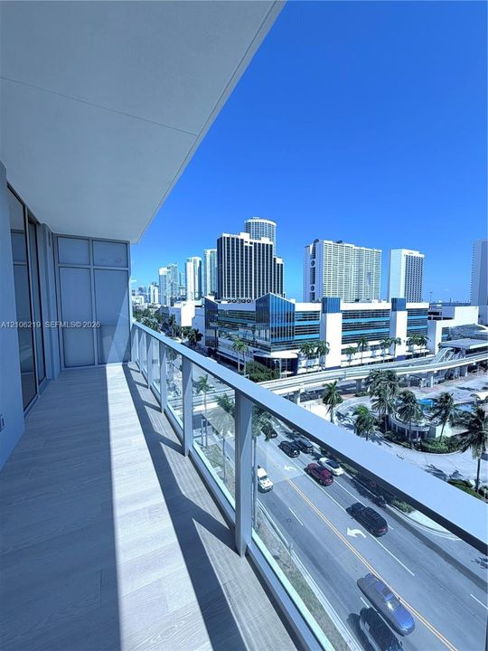 Covered balcony featuring wood-finish flooring and glass panel railing with metal frame