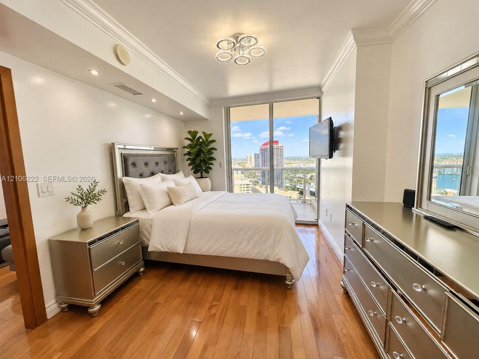 Wood-finish flooring, crown molding, recessed lighting, multi-bulb ceiling fixture, and floor-to-ceiling glass doors opening to a balcony