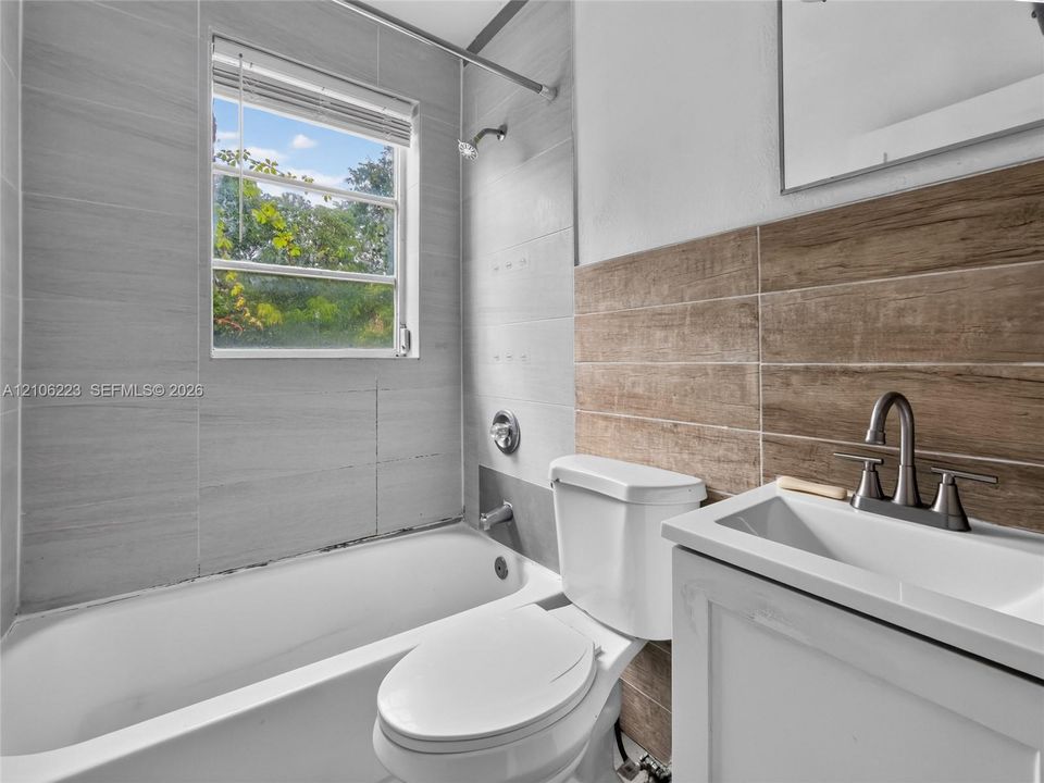 Bathroom featuring grey wall tile, wood-finish tile accents, a porcelain tub with shower head, and a white vanity with a metal faucet