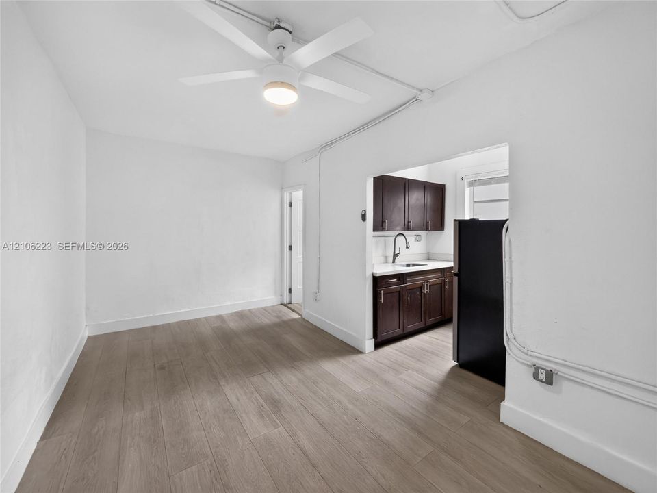 Interior space featuring wood-finish flooring, a white ceiling fan with integrated lighting, and a kitchenette equipped with dark-finish cabinetry, solid-surface countertops, and a single-basin sink