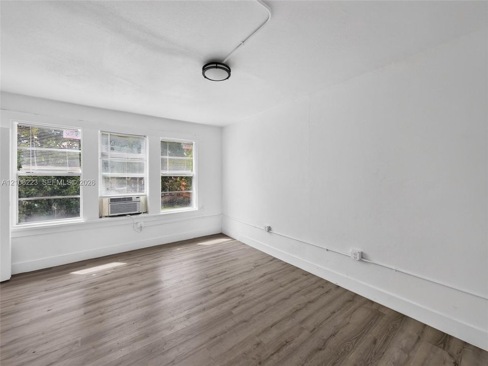 Interior space featuring wood-finish flooring, white walls, triple window configuration, and flush-mount ceiling lighting