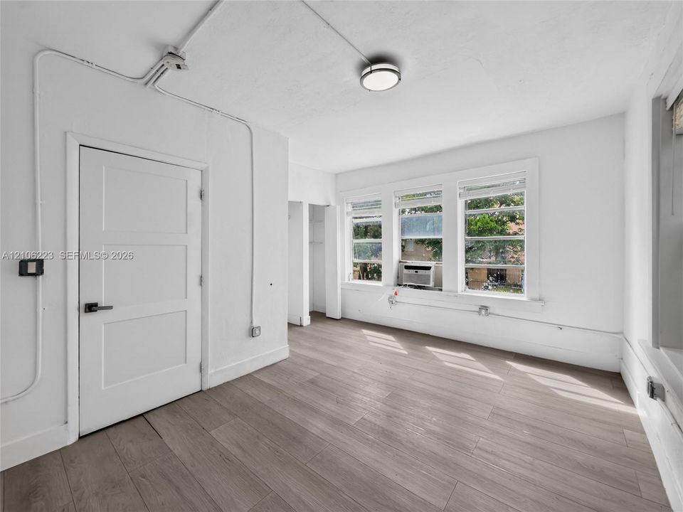 Neutral-toned wood-finish flooring, three paneled windows with natural light, a white three-panel door with modern hardware, and flush-mount ceiling lighting