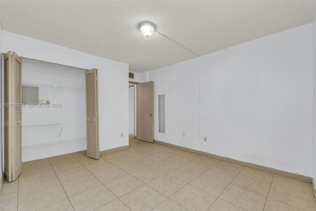 Neutral-toned tile flooring, closet with bi-fold louvered doors, and ceiling-mounted light fixture