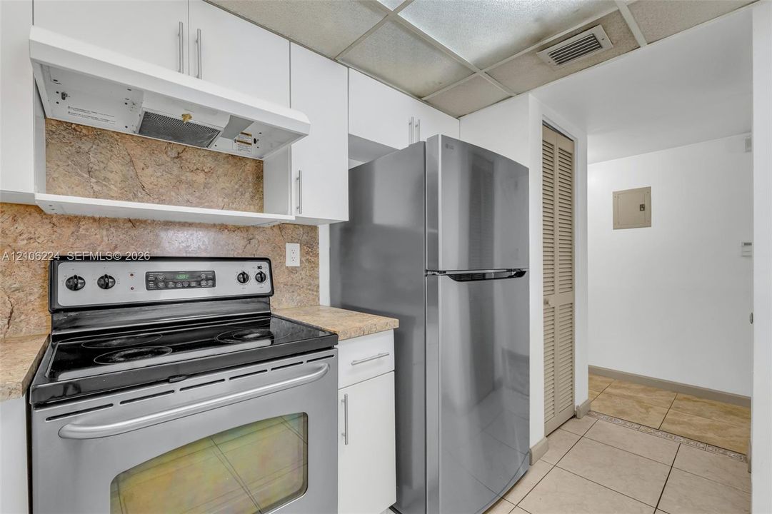 Kitchen featuring white cabinetry, stainless steel appliances, stone-finish countertops, tiled backsplash, and ceramic floor tile