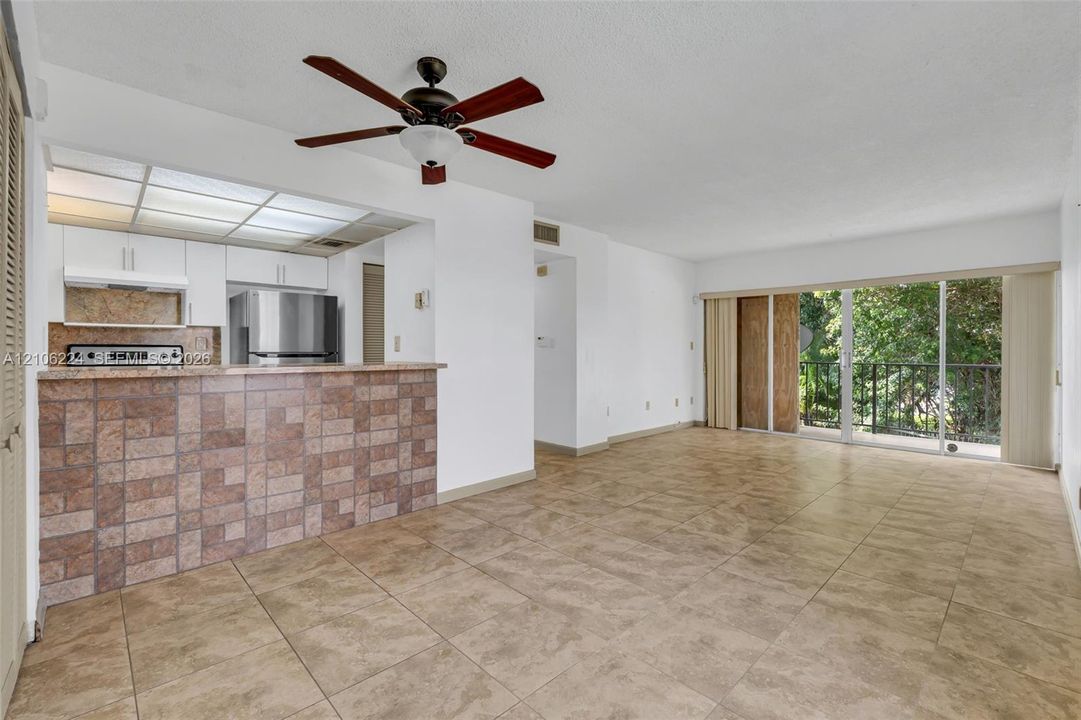 Open-concept living space featuring ceramic tile flooring, a breakfast bar with tiled surround, stainless steel appliances, a ceiling fan, and sliding glass doors leading to a balcony