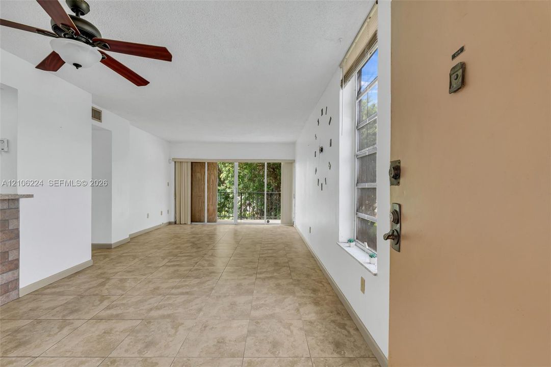 Interior space featuring ceramic tile flooring, a multi-blade ceiling fan, vertical window blinds, and sliding glass doors with exterior access