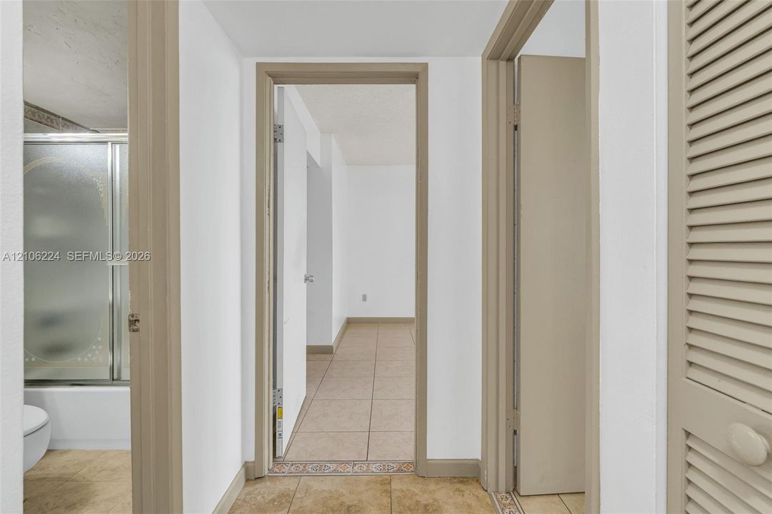 Hallway featuring neutral-tone tile flooring, neutral wall finishes, and a louvered closet door