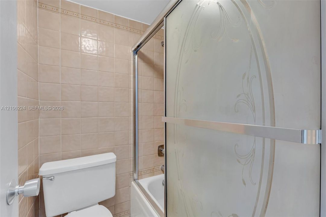 Full-height square wall tile, sliding shower door with decorative etched detailing, and integrated bathtub