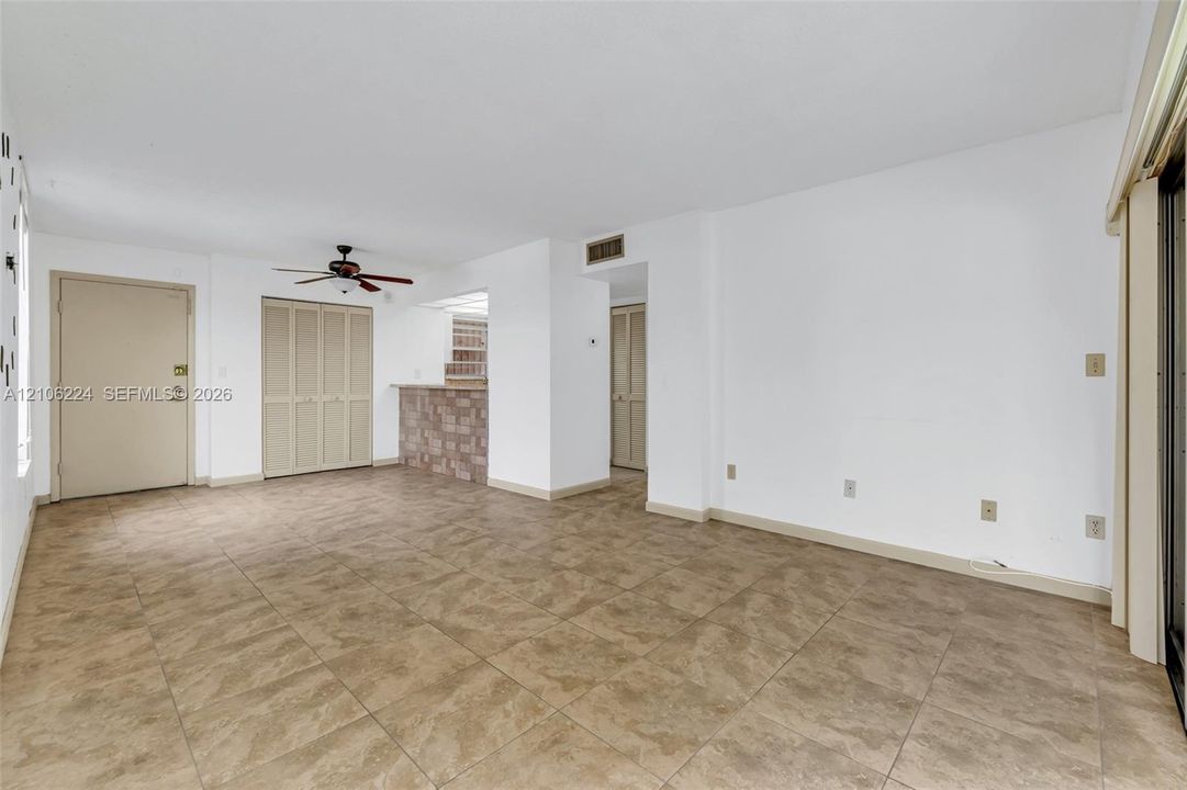 Open interior space featuring tile flooring, a stone-accented breakfast bar, a ceiling fan with light fixture, and bi-fold closet doors