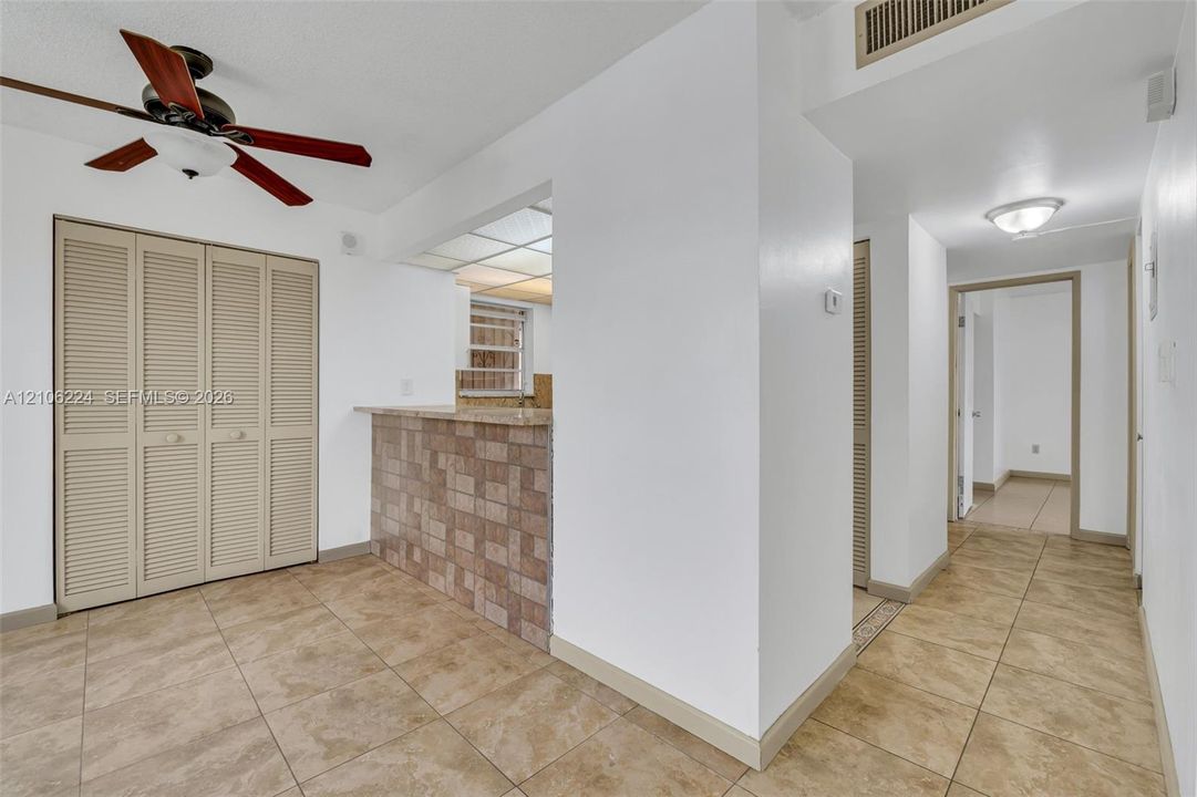 Tile flooring, pass-through counter with tiled facade, ceiling fan with light fixture, and floor-to-ceiling louvered closet doors
