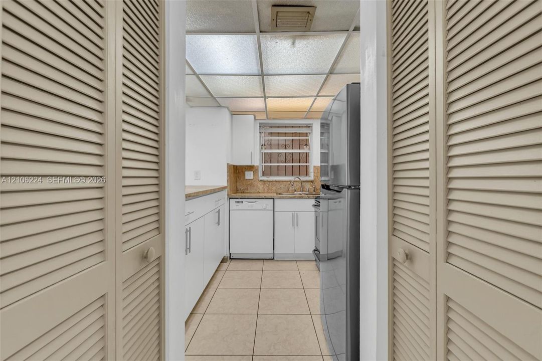 Kitchen area featuring white cabinetry, light-toned stone-finish countertops, stainless steel appliance suite, tile flooring, and louvered closet doors