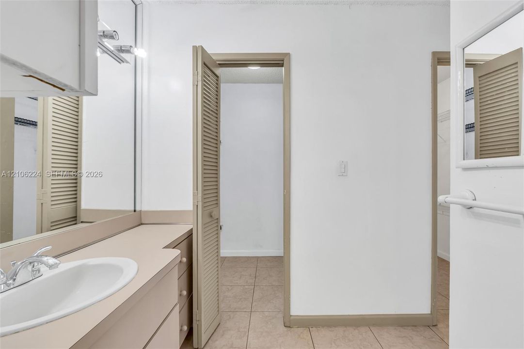 Vanity featuring a neutral countertop with an integrated oval basin, full-width mirror, louvered closet doors, and tile flooring