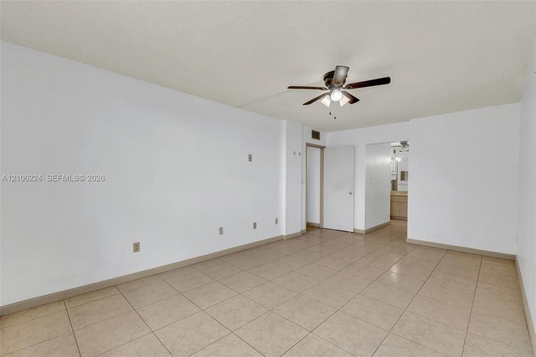 Interior space featuring neutral-toned tile flooring, white walls, and a ceiling-mounted light fixture with a multi-blade fan