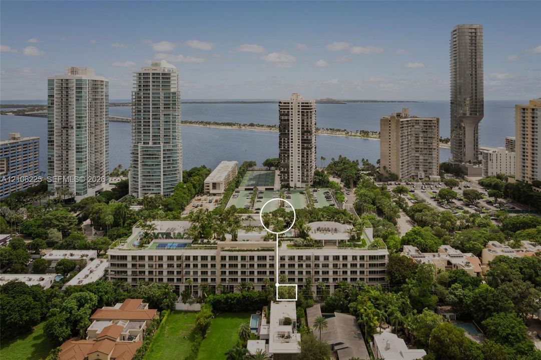 Aerial perspective of a multi-story residential building featuring rooftop recreational facilities, landscaped gardens, multiple tennis courts, and mature perimeter trees