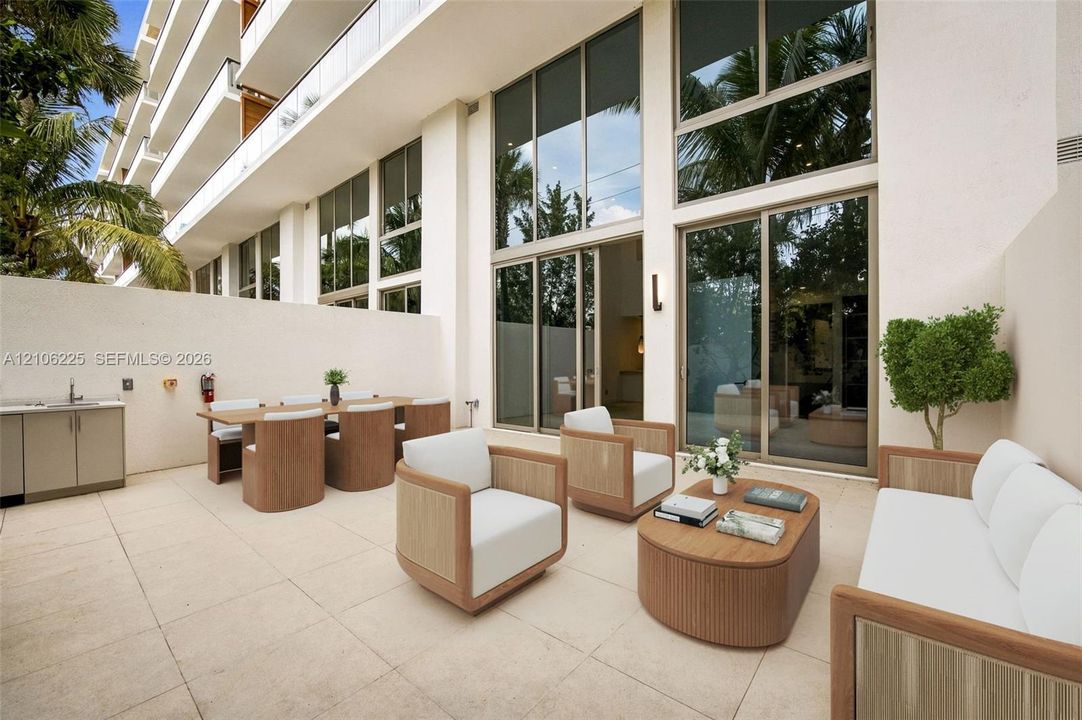 Private patio featuring light-toned stone paving, floor-to-ceiling windows, integrated exterior cabinetry, and a stainless steel sink