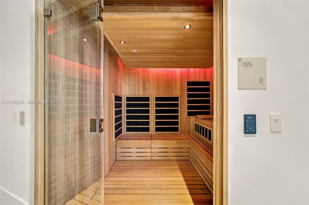 Sauna room featuring light wood-paneled walls and flooring, integrated heating elements, recessed lighting, and a glass door with a polished metallic handle