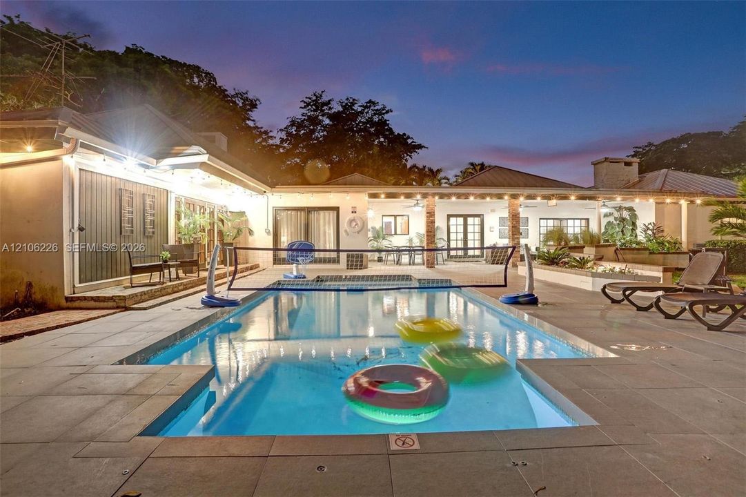 Rectangular swimming pool with stone paver surround, covered patio, exterior masonry chimney, and recessed ceiling lighting