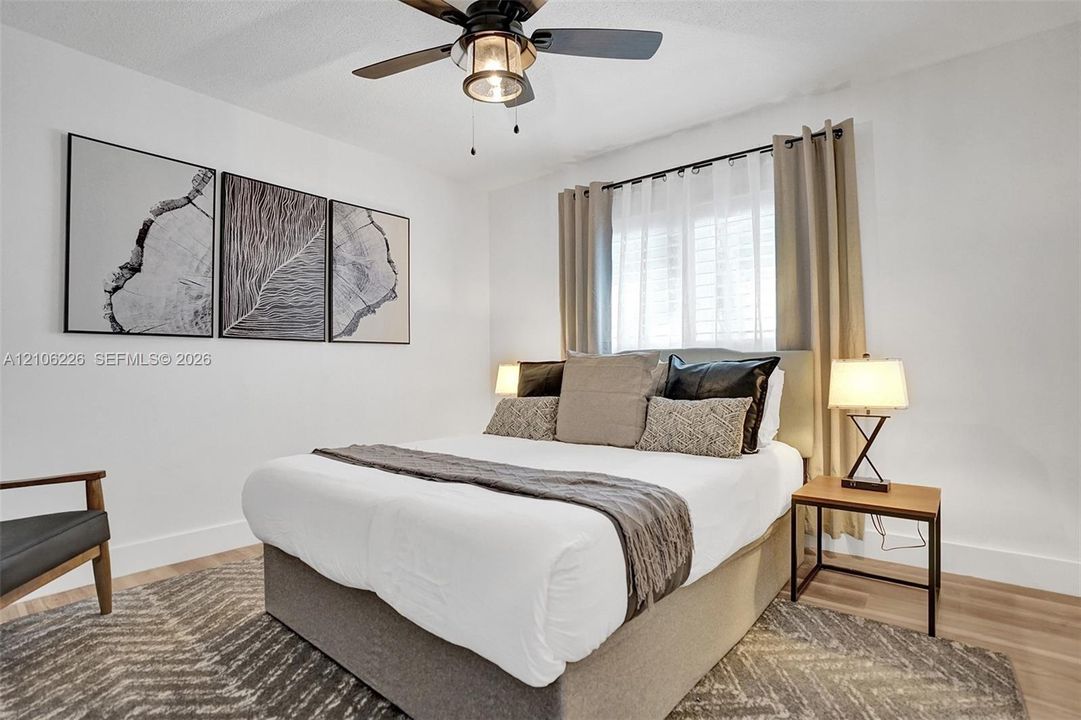 Neutral-toned room featuring wood-finish flooring, a multi-blade ceiling fan with integrated lighting, and a window with plantation-style shutters