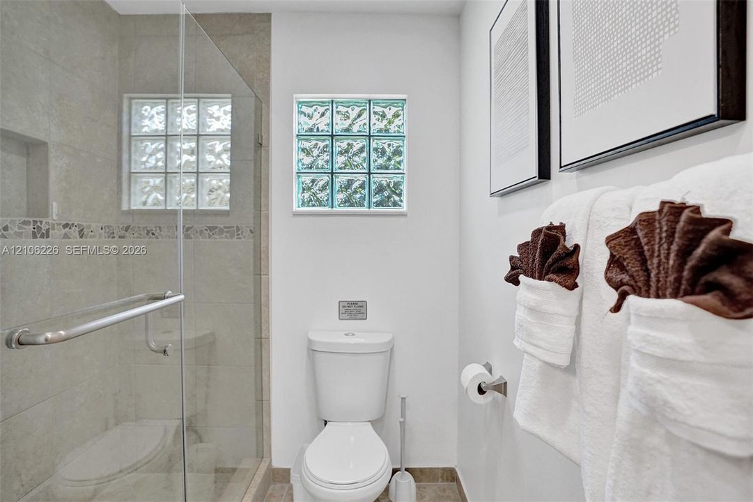 Walk-in shower with a glass enclosure, neutral tile surround, and built-in recessed niche, complemented by glass block windows and tile flooring