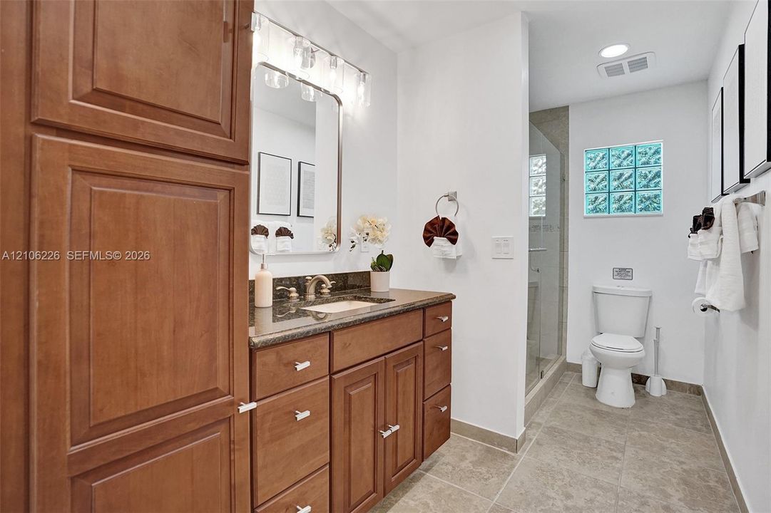 Bathroom featuring a wood-finish vanity with stone countertop, drop-in sink, glass block window, and a walk-in shower with glass enclosure